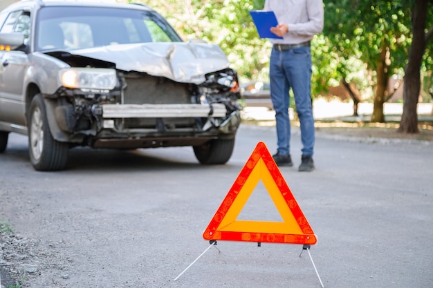 Agente de seguros de homem descreve evento segurado com carro destruído após acidente de carro. Seguro automóvel na estrada. Homem com tablet fazendo leituras após o acidente. Carro quebrado na estrada.