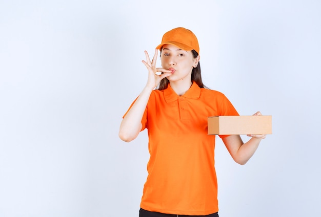 Agente de serviço feminino com código de vestimenta cor de laranja segurando uma caixa de papelão e mostrando sinal de sucesso