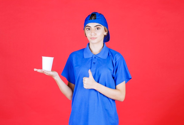 Agente de serviço feminino de uniforme azul, segurando um copo descartável de bebida e apreciando o sabor.