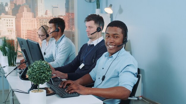 Foto agente de suporte ao cliente preto trabalhando em um call center ocupado, conversando com o cliente internacional