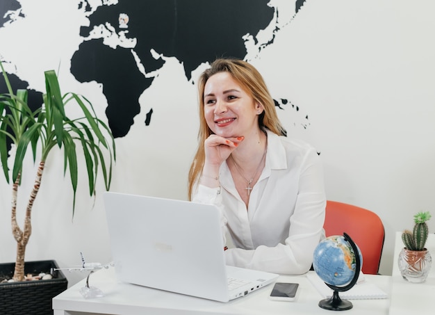 Agente de viagens confiante usando laptop no escritório sobre o mapa para comunicação online
