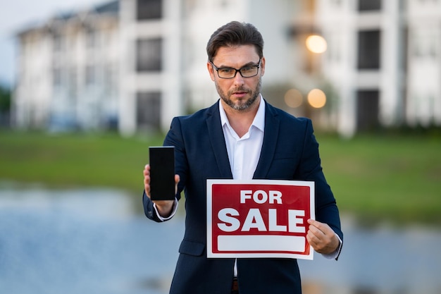 Foto agente imobiliário de sucesso em terno com sinal de venda corretor imobiliário em frente à casa nova imobiliária