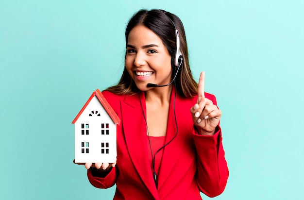 Agente imobiliário de uma jovem hispânica com um modelo de casa e fone de ouvido