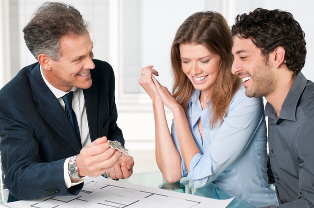 Foto agente inmobiliario feliz mostrando nuevas llaves de casa a una joven pareja después de una discusión sobre los planos de la casa.