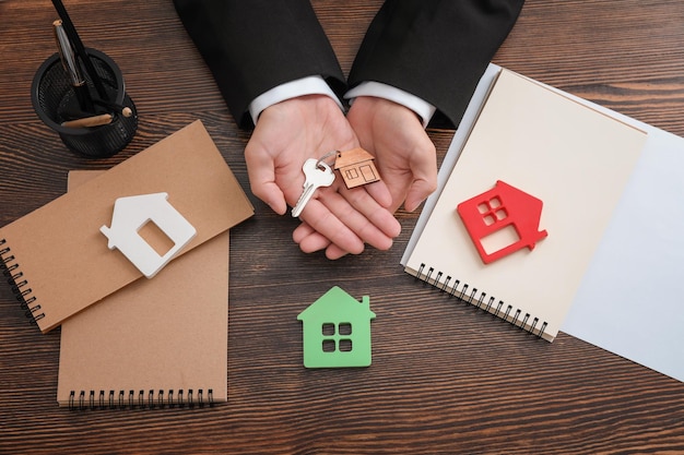 Foto agente inmobiliario con modelos de casas clave y cuadernos en la mesa.