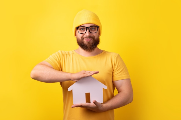El agente inmobiliario que tiene la casa sobre fondo amarillo, el concepto de compra, venta o alquiler de una casa
