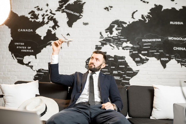 Agente masculino guapo jugando con avión de juguete en la oficina de la agencia de viajes con mapa del mundo en el fondo