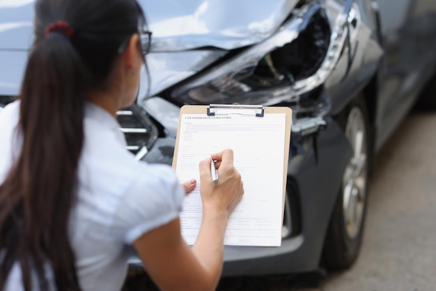 Agente de la mujer llenando el formulario de reclamación de seguros cerca del primer coche destrozado llenando el seguro