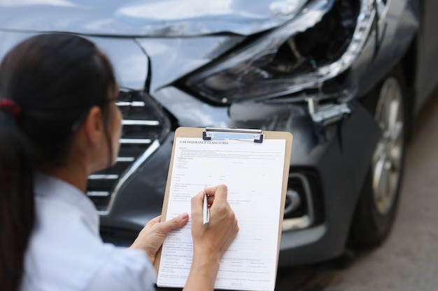 Foto la agente de seguros de la mujer completa el formulario de seguro por daños en el automóvil después de la inspección de un accidente de tráfico