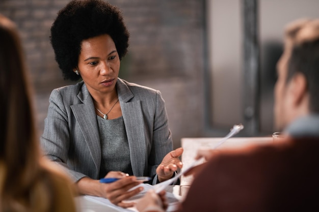 Agente de seguros mujer negra hablando con una pareja mientras revisa los términos de un contrato durante la reunión