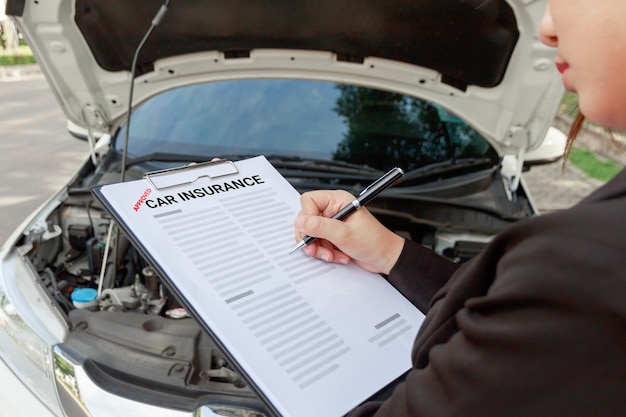 Agente de seguros que escribe en el documento de seguro de automóvil y que examina el coche después de accidente.