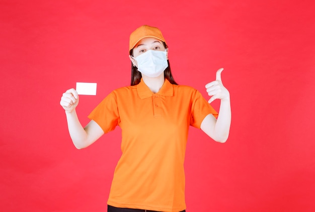 Agente de servicio femenino en código de vestimenta de color naranja y máscara que presenta su tarjeta de visita y muestra un signo de mano positivo