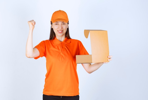 Agente de servicio femenino en código de vestimenta de color naranja sosteniendo una caja de cartón abierta y mostrando un signo de mano positivo