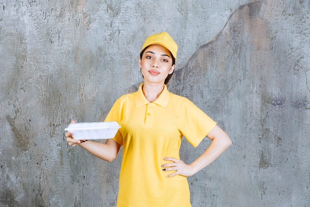 Agente de servicio femenino en uniforme amarillo sosteniendo una caja de comida para llevar de plástico