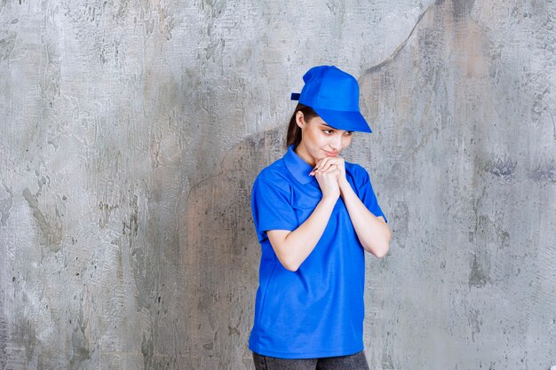 Agente de servicio femenino en uniforme azul poniendo la mano en el pecho y parece confundida o pensativa.