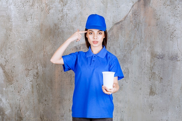 Foto agente de servicio femenino en uniforme azul sosteniendo un vaso desechable blanco y parece pensativo.