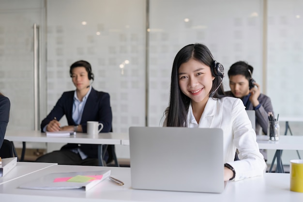 Agente de servicios al cliente femenino joven hermoso con el auricular que trabaja en una oficina del centro de atención telefónica. concepto de atención al cliente del equipo de servicio al cliente