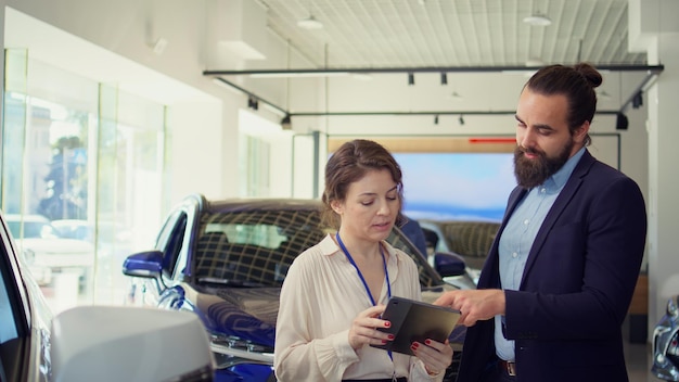 Agente usando dispositivo para ajudar o homem a avaliar carros na concessionária antes de comprar