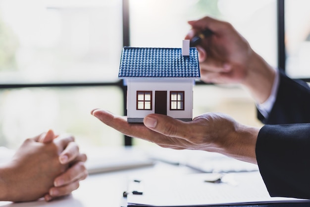 Los agentes inmobiliarios acuerdan comprar una casa y dar llaves a los clientes después de firmar el acuerdo de contrato en la oficina mudándose a casa o alquilando una propiedad