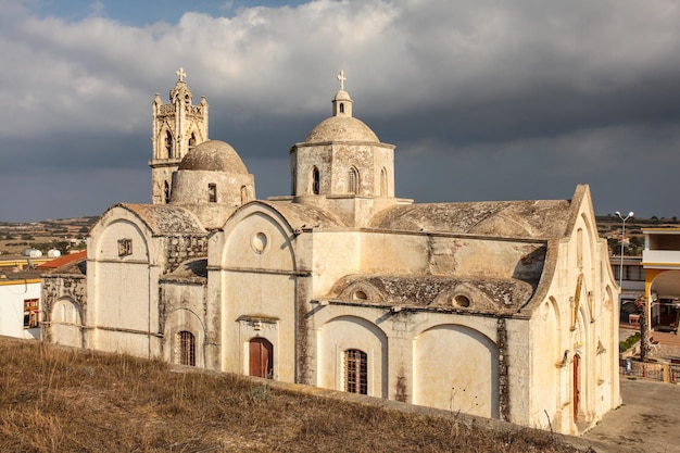 Agios-Synesios-Kirche in Rizokarpaso (Dipkarpaz), beleuchtet von der Nachmittagssonne, einige schwere Wolken im Hintergrund. Diese Stadt im Norden Zyperns ist bekannt für das harmonische Zusammenleben von Christen und Muslimen.