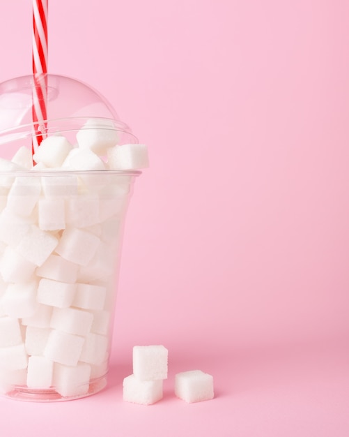 Agite o copo cheio de cubos de açúcar no fundo rosa Conceito de ingestão excessiva de açúcar