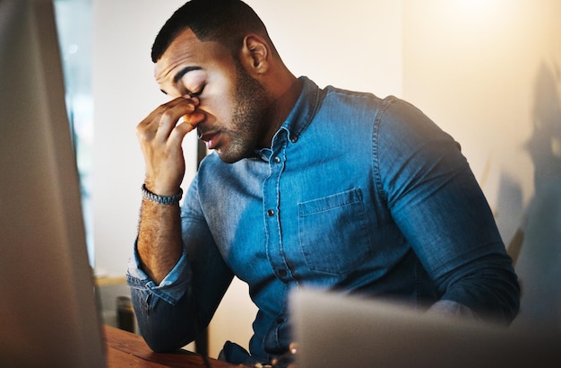 Agotamiento de la migraña y hombre de negocios que trabaja en la oficina por la noche con una computadora para investigación corporativa Dolor de cabeza por estrés y empleado africano profesional que trabaja horas extra en un proyecto de fecha límite en el lugar de trabajo