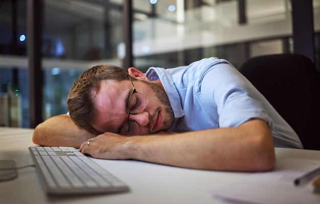 Agotamiento del negocio del sueño nocturno y hombre de negocios durmiendo en su escritorio en su oficina oscura en el trabajo Trabajador o gerente corporativo cansado con estrés tomando una siesta en una mesa mientras trabaja horas extras