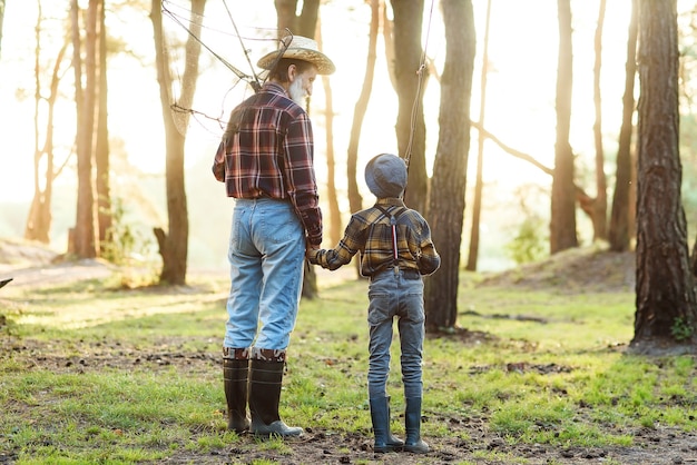 Agradable abuelo barbudo confiado en el bosque yendo a pescar junto con su nieto de 10 años y hablando de pesca.