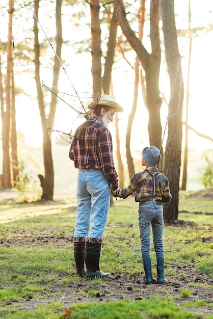 Agradable abuelo barbudo confiado en el bosque yendo a pescar junto con su nieto de 10 años y hablando de pesca.