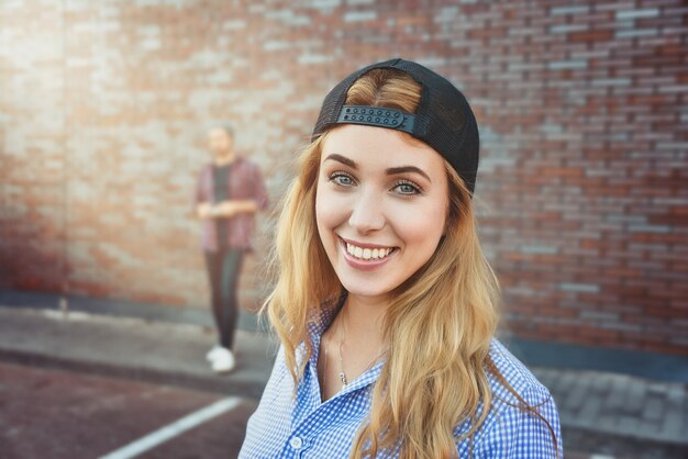 Agradable adolescente caucásico viste camisa y gorra negra, va a dar un paseo con amigos, posa contra la superficie blanca. Mujer joven vestida con ropa de moda.