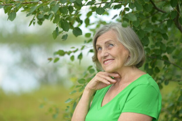 Agradable anciana sonriente en el fondo de hojas verdes