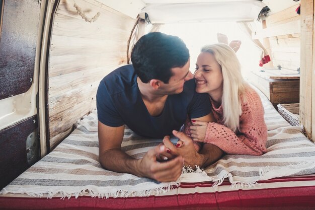 Agradable y atractiva joven pareja milenaria enamorada se acuesta en la cama dentro de una pequeña y acogedora camioneta perfecta para viajar y disfrutar de las vacaciones alternativas de la vida en camioneta alrededor del mundo.