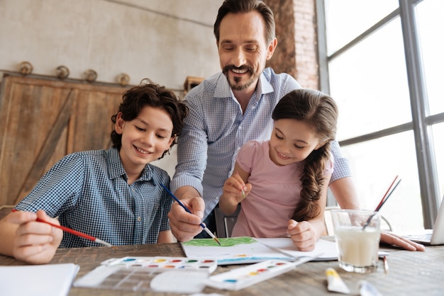 Foto agradable familia alegre que parece feliz mientras se unen entre sí y crean una hermosa pintura de acuarela juntos.