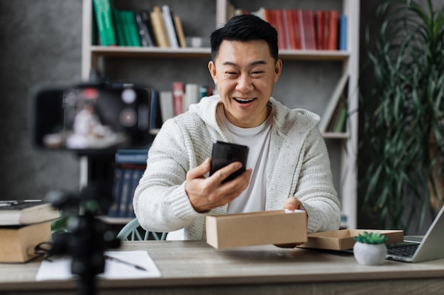 Agradable hombre asiático abriendo caja de paquetes con un nuevo teléfono inteligente