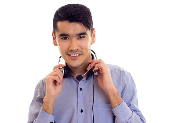 Agradable joven con cabello oscuro en camisa azul con auriculares negros sobre fondo blanco en estudio