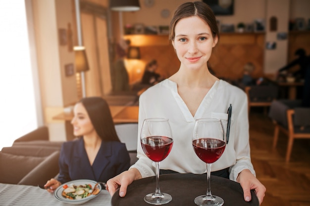 Agradable joven camarera con bandeja de copas de vino tinto