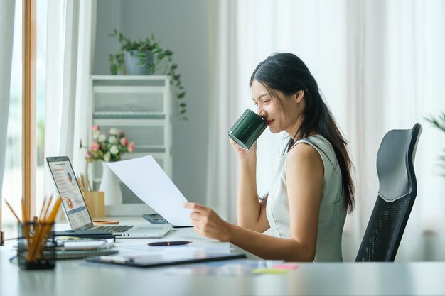 Agradable joven disfrutando de su café matutino mientras está sentada en su lugar de trabajo