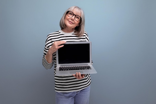 Agradable y sonriente mujer de mediana edad que muestra una página web de maquetas en una laptop con un brillante fondo de estudio