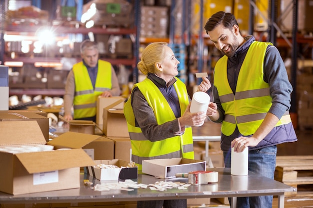 Agradable trabajador de almacén sonriendo y mirándose mientras coloca etiquetas en los productos