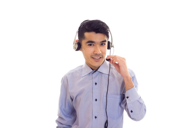 Agradável jovem com cabelo preto na camisa azul com fones de ouvido pretos sobre fundo branco no estúdio