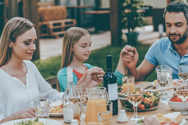 Agradecendo pela refeição. família de mãos dadas e orando antes do jantar enquanto está sentado à mesa ao ar livre