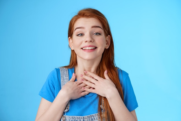 Agradecida, sincera, linda encantadora pelirroja mujer agradeciendo a sus amigos, sonriendo encantada apreciar un bonito gesto tierno, presionar las palmas del corazón del pecho, agradecido, mirar admiración y amor, soporte fondo azul