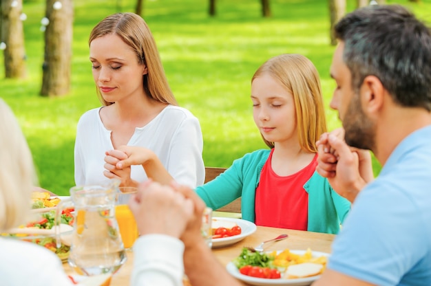 Agradeciendo a Dios por la comida. Familia tomados de la mano y rezando antes de la cena mientras está sentado en la mesa al aire libre