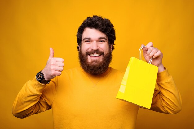 Agradezco la oportunidad de comprar en línea. El hombre sonriente está mostrando el pulgar hacia arriba y la bolsa de papel amarilla.