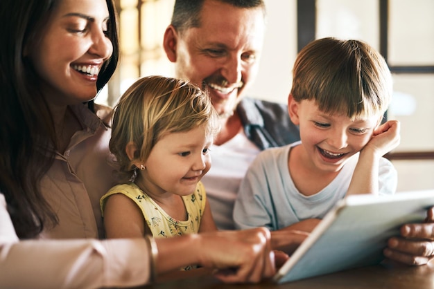 Agregando tiempo frente a la pantalla al tiempo en familia Foto de una familia joven de cuatro integrantes usando una tableta digital juntos en casa