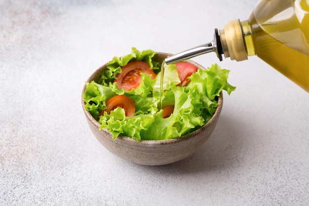 Agregar aceite de oliva en un tazón con ensalada de vegetales frescos Alimentos crudos y vegetarianos en la sociedad moderna vegano es un concepto popular