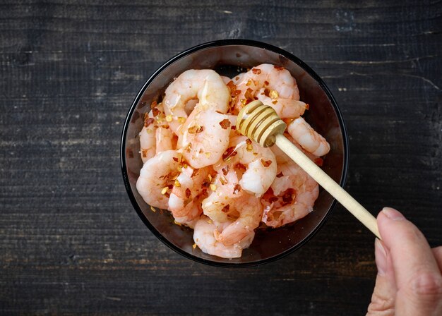 Agregar miel al tazón de gambas y hojuelas de chile en la mesa de la cocina de madera negra