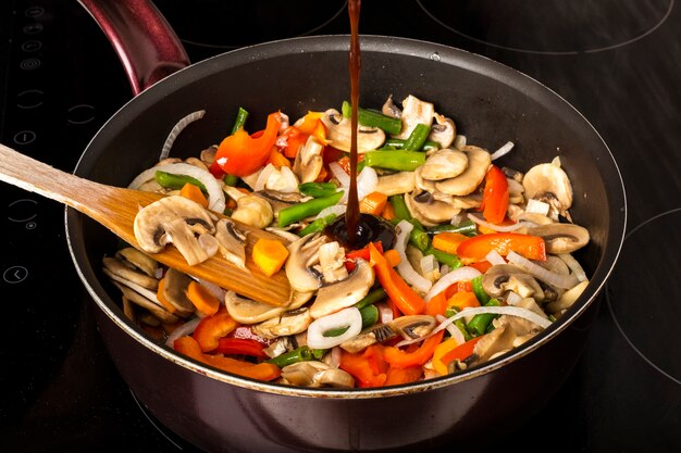 Agregar salsa a las verduras fritas con champiñones en una sartén sobre un fondo oscuro