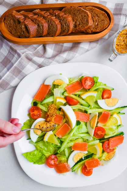 Foto agregue mostaza a la ensalada de verduras. ensalada de verduras con manos humanas. en un plato blanco añadir especias