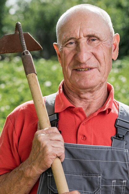 Un agricultor adulto con una azada posando en el fondo de la granja